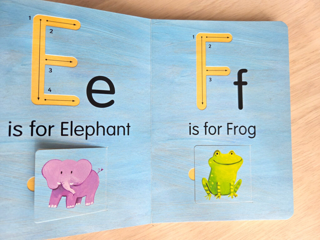 「Hello World! ABCs」のEとFのページ。左ページには紫色のゾウのイラストと「is for Elephant」、右ページには緑色のカエルのイラストと「is for Frog」と書かれている。ゾウとカエルのイラストはめくれる仕掛け(扉)になっており、この画像では仕掛けが閉じている状態。