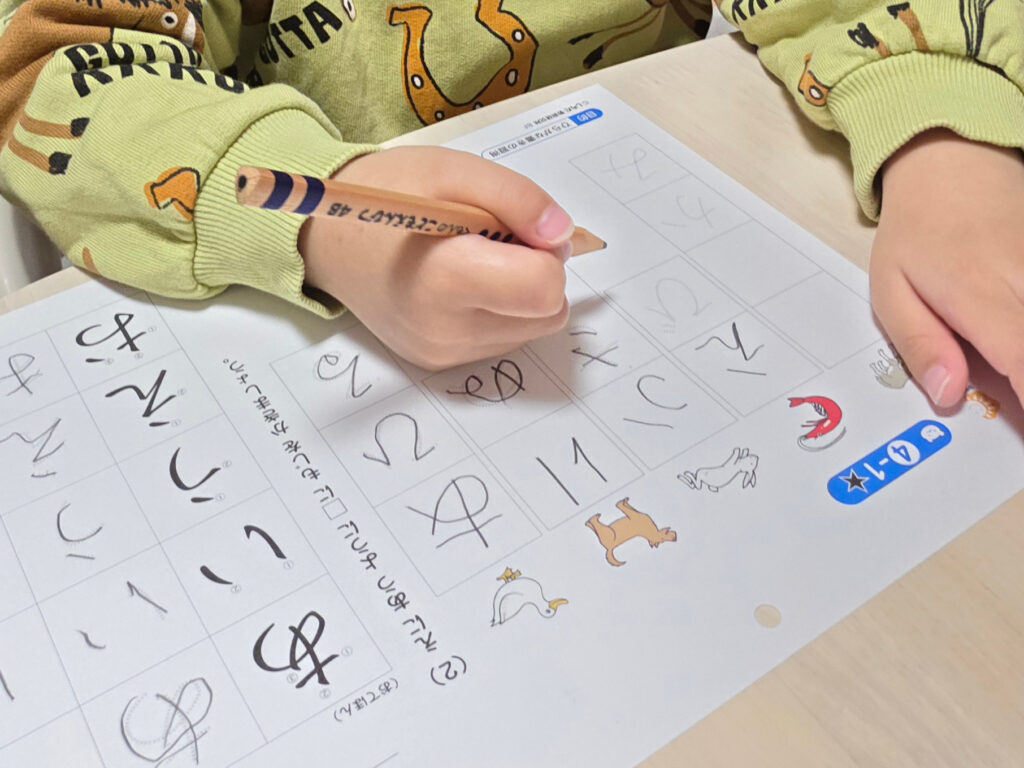 こどもえんぴつを使い、真剣な手つきで「ひらがな」の練習帳に取り組む4歳息子の手元