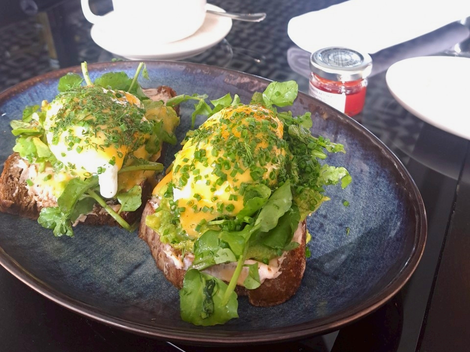 57階「Spago」のアラカルト朝食。シックな色合いのお皿に、たっぷりのアボカドとハーブ、そして完璧な形をした2つのポーチドエッグが美しく盛り付けられたアボカドトースト。